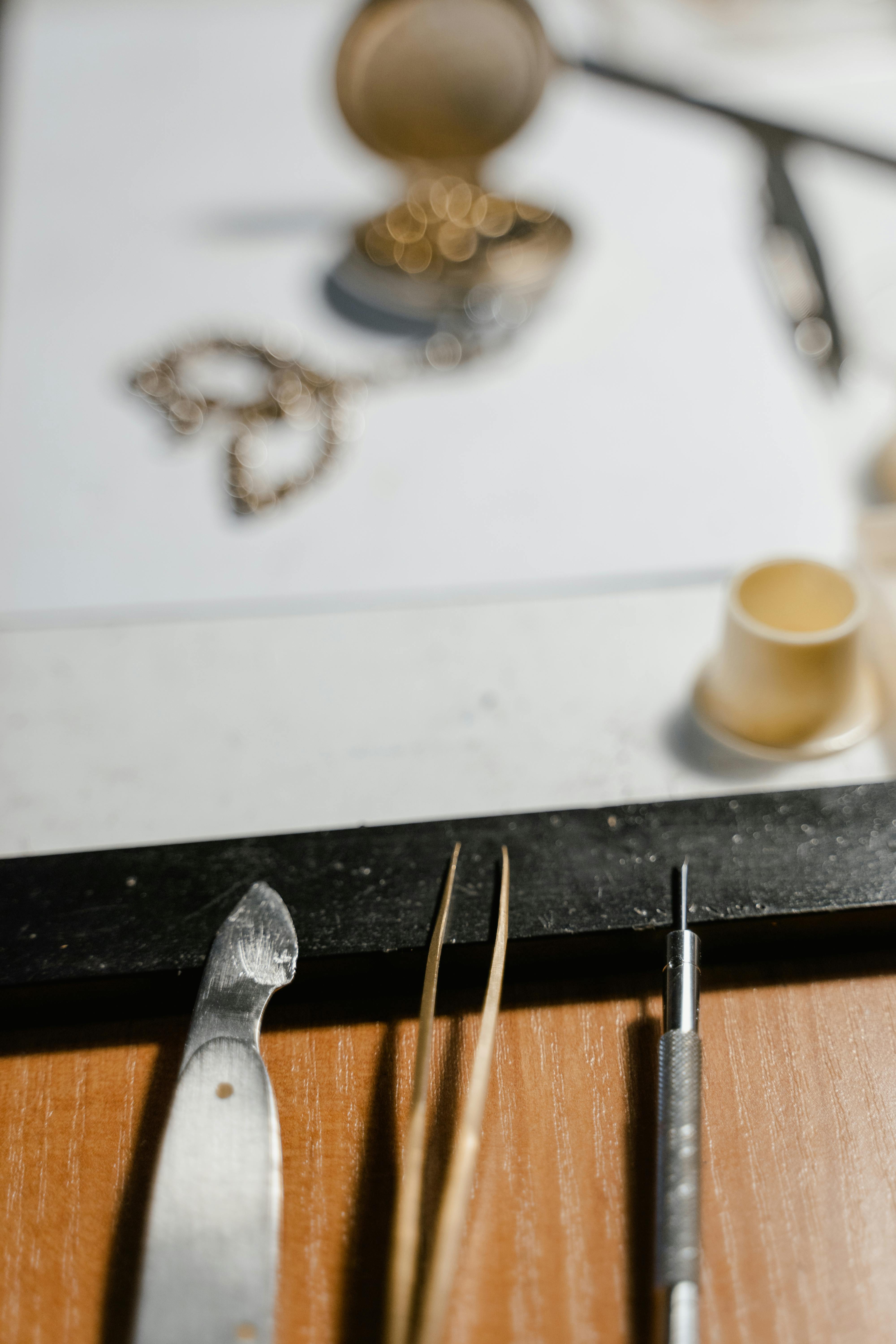 Close-up of a case knife, precision tweezers, and screwdriver resting at the edge of a workbench